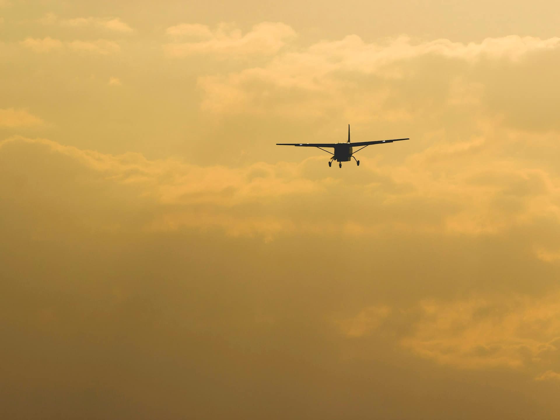 A small high-wing airplane flying toward the camera through golden evening haze