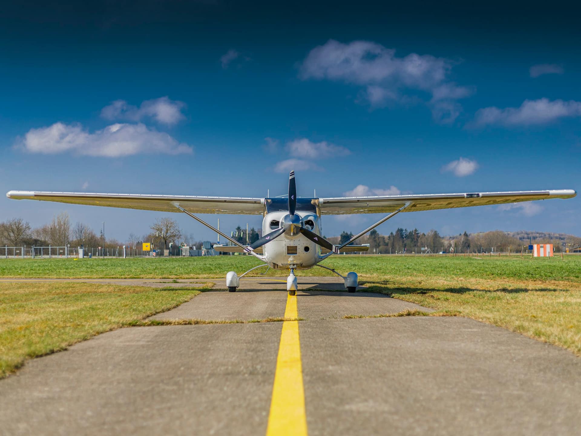 A white Cessna 172 on a taxiway centreline, facing the camera under a blue sky with scattered clouds